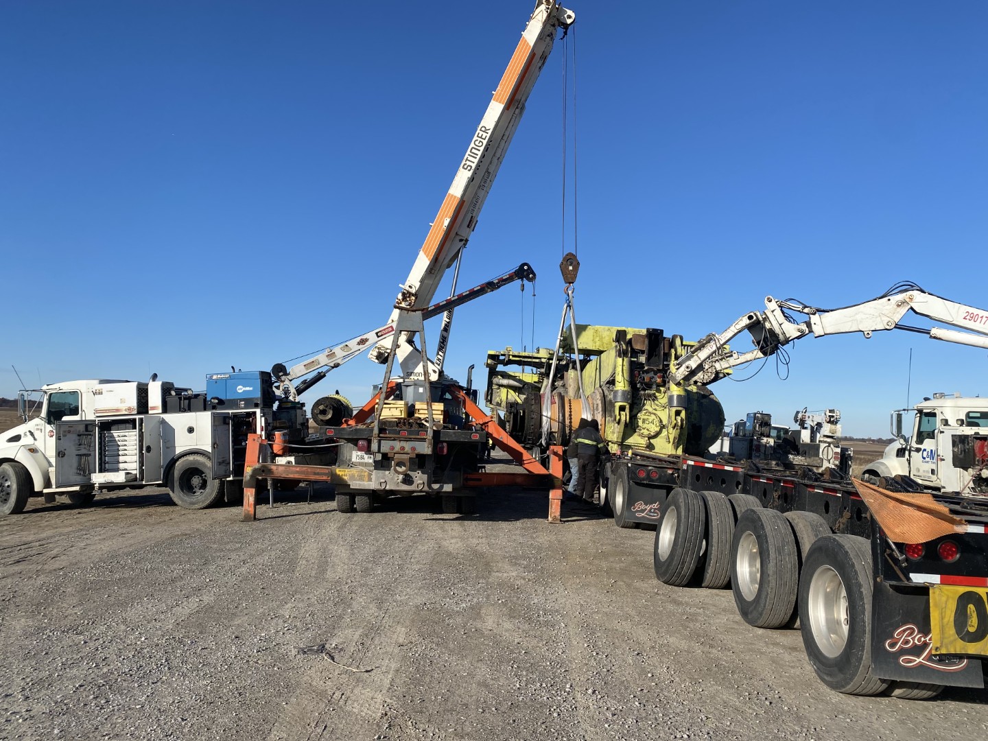 crane lifting heavy equipment onto lowboy